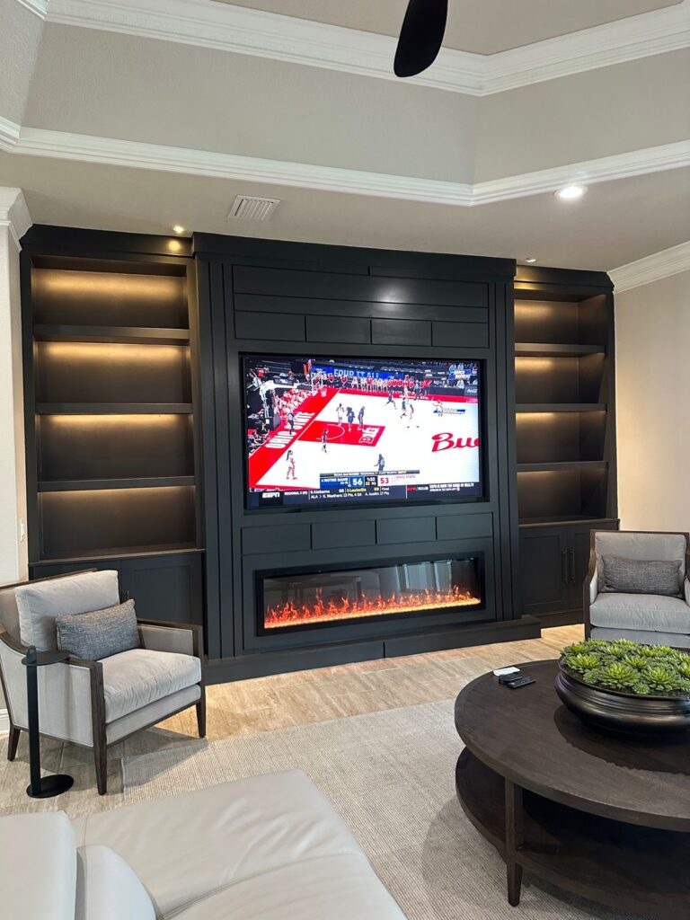 Custom black built-in TV wall with electric fireplace, illuminated shelving and cabinetry in a luxury living room. Modern media wall design installed in Orlando, Florida.