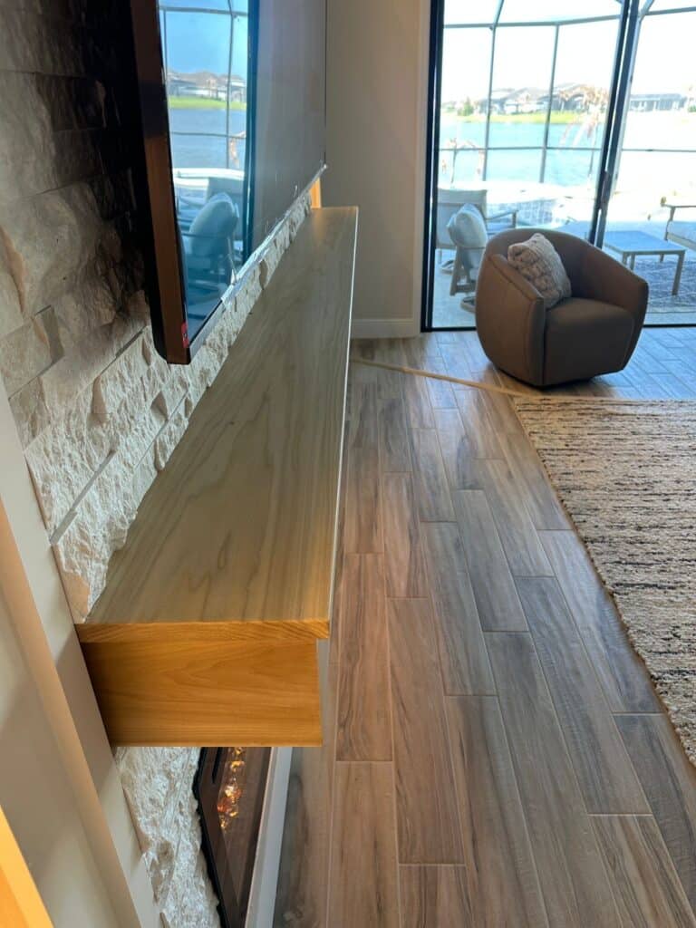 Side view of luxury custom fireplace TV wall with floating wood mantel, stone finish and modern built-in media wall in Florida home