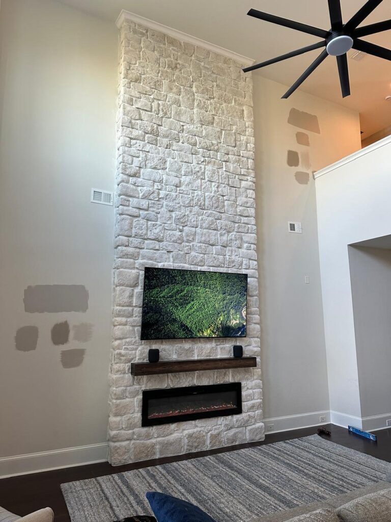 Tall white stone fireplace wall with mounted TV, floating wood mantel and modern electric fireplace in luxury Florida living room